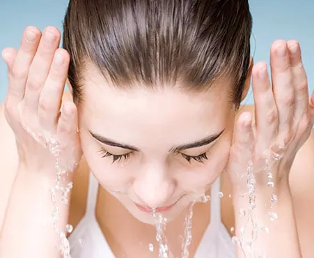 Frau wäscht sich mit Wasser das Gesicht